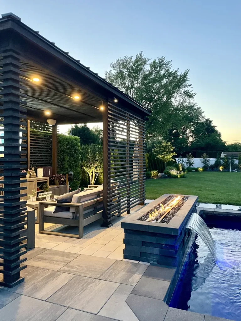 Pool Terrasse mit Naturstein und dunklem Holz. Mit Wasserfall der in den Pool fließt.